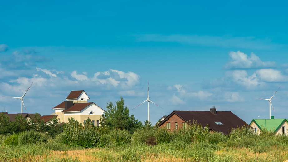 Wind turbines behind houses in residential area on blue sky background